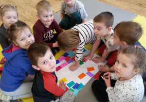 Widok na grupę dzieci zgromadzonych wokół białego kartonu z kolorowymi karteczkami.